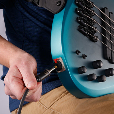 Person plugging a cable into a blue electric guitar