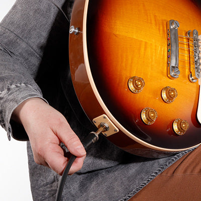 Person holding a sunburst electric guitar with a cable plugged into it on a white background