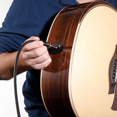 Person plugging an audio cable into a guitar on a white background