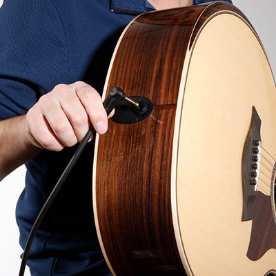 Person holding an acoustic guitar and plugging an audio cable in