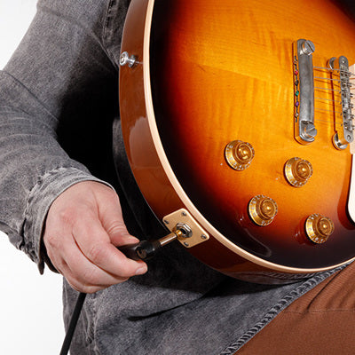 Person holding a sunburst electric guitar with a white background and plugging in a cable