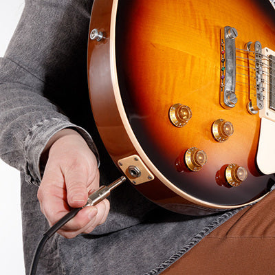 Person holding a sunburst electric guitar with a cable plugged in, on a white background
