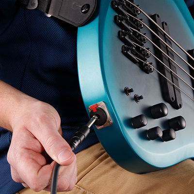 Person plugging ia cable in a blue bass guitar