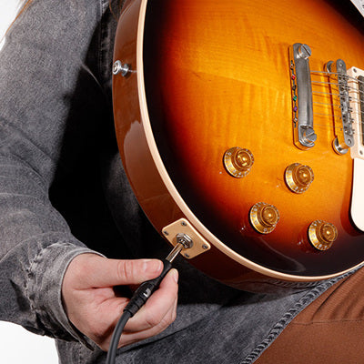 Person holding a sunburst electric guitar with a close-up of the body and a hand plugging in a cable.