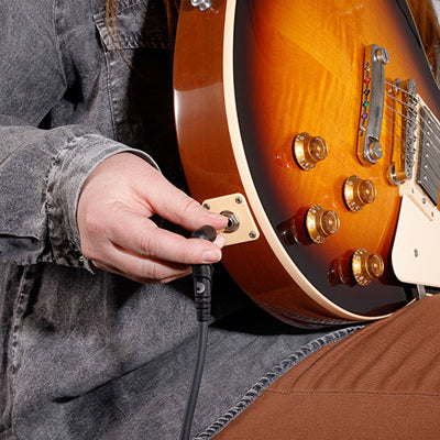 Person plugging a cable into an electric guitar