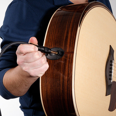 Person plugging an acoustic guitar into a device with a white background