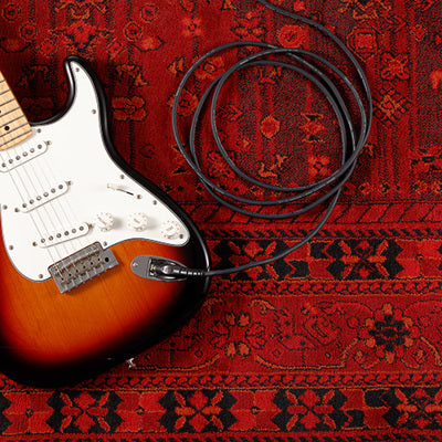 Electric guitar with a coiled cable on a red patterned rug