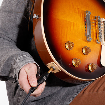 Person holding a sunburst electric guitar with a cable plugged into the jack.