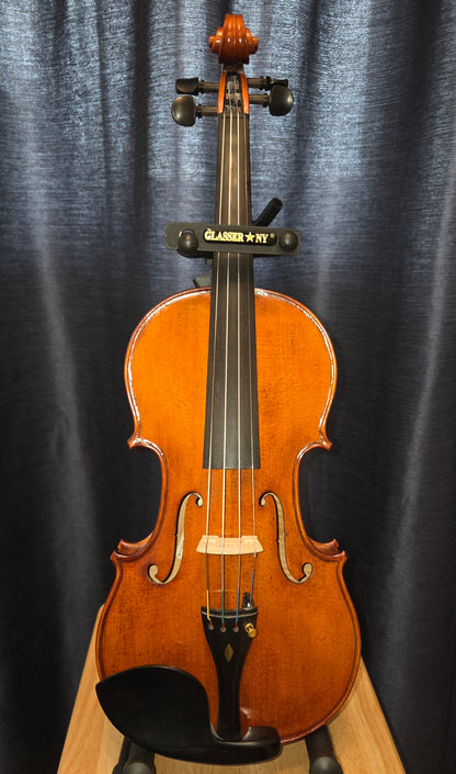 A classic wooden violin with a glossy orange-brown finish, displayed upright on a stand against a dark blue-gray curtain backdrop.