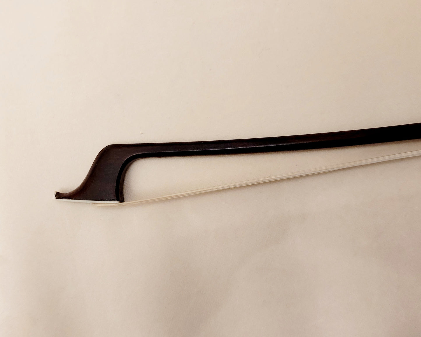 The tip end of a cello bow on a beige background.