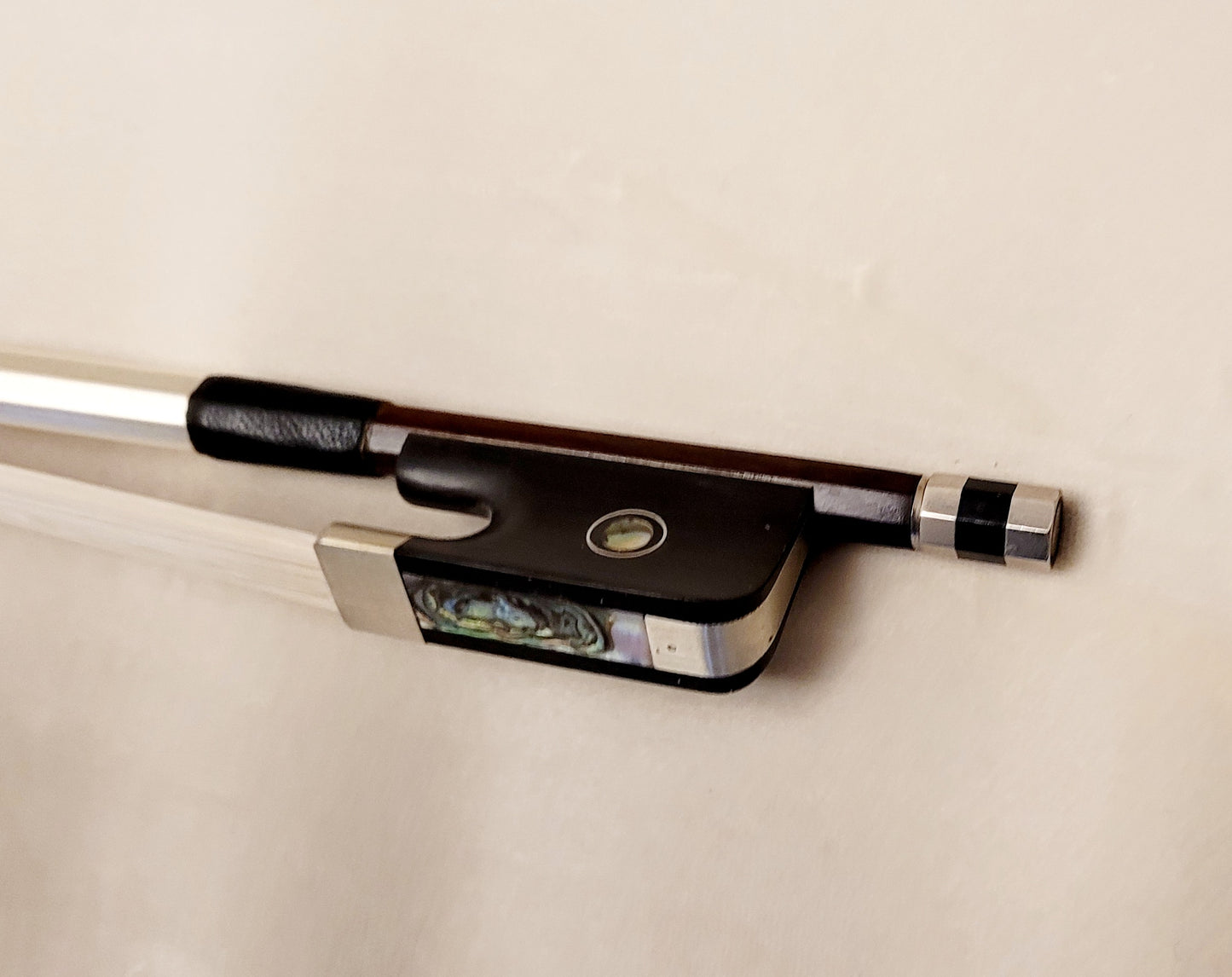 Cello bow on a white background - ebony frog with Parisian eye, nickel mounting and Mother-of-pearl slider.