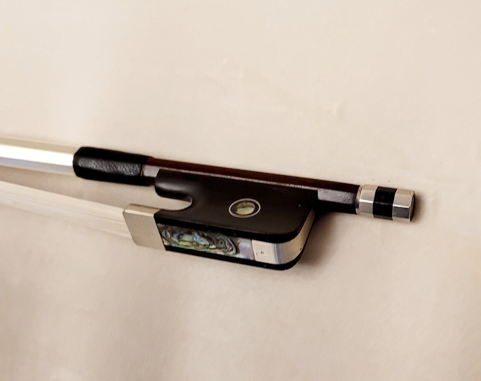 Cello bow on a white background - ebony frog with Parisian eye, nickel mounting and Mother-of-pearl slider.